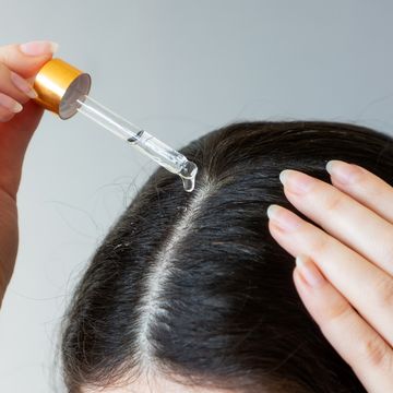 close up of a female head with dark hair woman using pipette with a cosmetic product near the hair parting the concept of dandruff