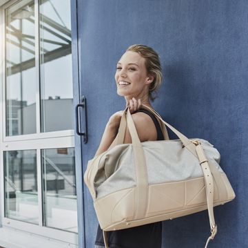 portrait of smiling young woman with sports bag in front of gym